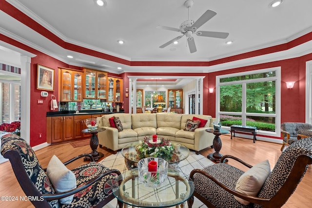 living room featuring decorative columns, light wood-style flooring, indoor wet bar, ceiling fan, and ornamental molding