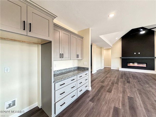 kitchen with a textured ceiling, gray cabinets, dark stone countertops, a fireplace, and dark hardwood / wood-style flooring