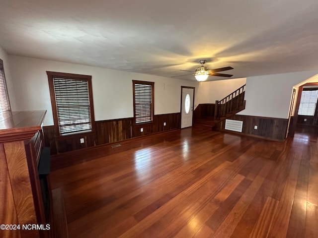 unfurnished room with ceiling fan, wooden walls, and dark wood-type flooring