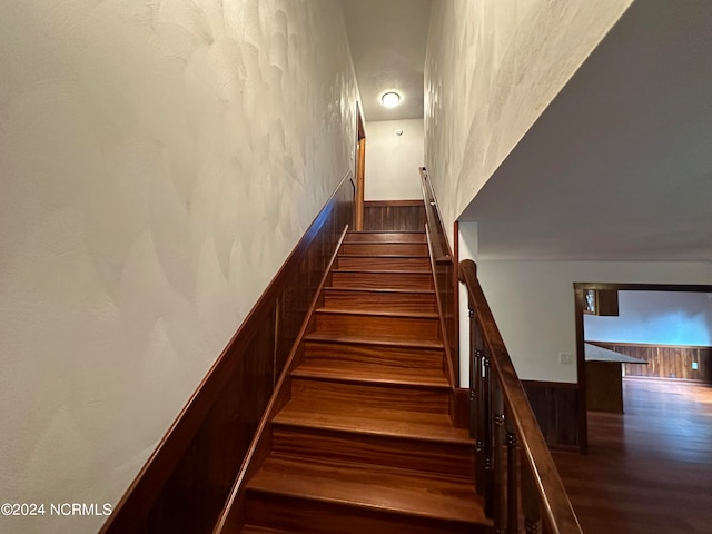 hallway with a textured ceiling, light hardwood / wood-style flooring, and wood walls