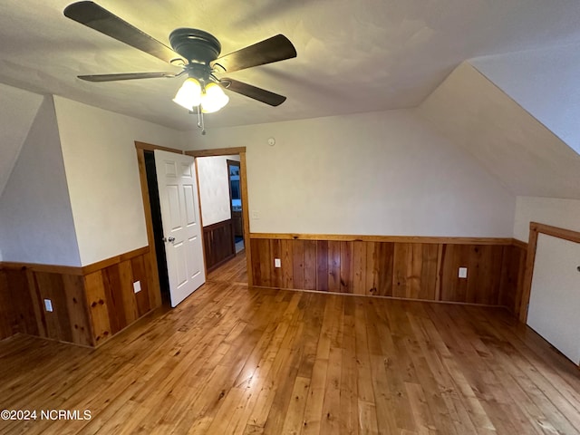 additional living space featuring wood walls, a textured ceiling, wood-type flooring, lofted ceiling, and ceiling fan