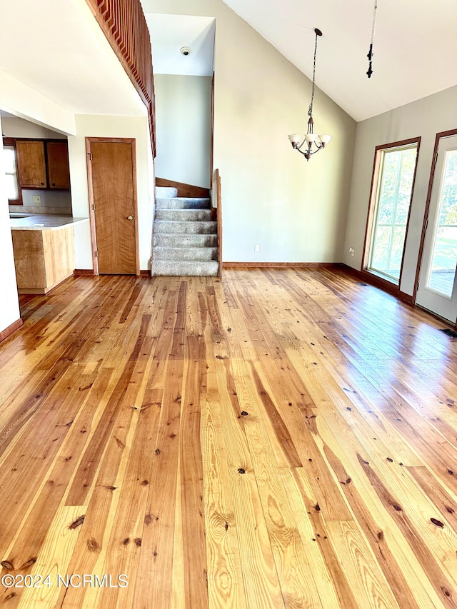 unfurnished living room featuring light hardwood / wood-style floors, vaulted ceiling, and a chandelier