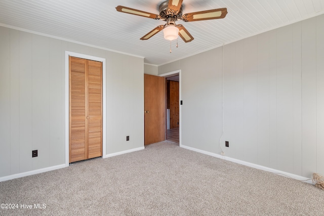 unfurnished bedroom featuring wood walls, ceiling fan, a closet, and carpet