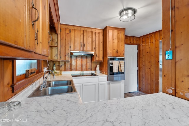 kitchen featuring stainless steel oven, wood walls, sink, white cabinets, and black electric cooktop