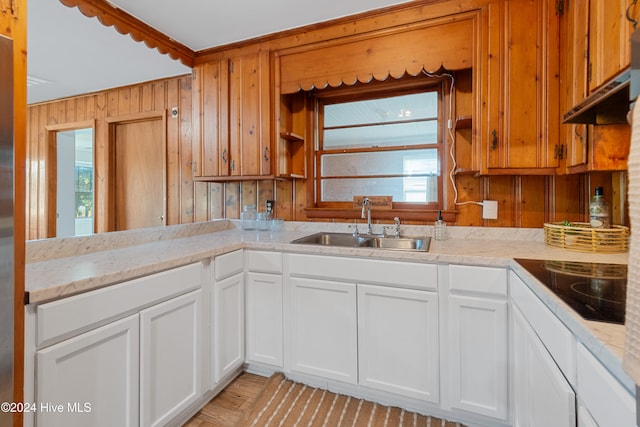 kitchen with white cabinets, wood walls, sink, and black electric cooktop