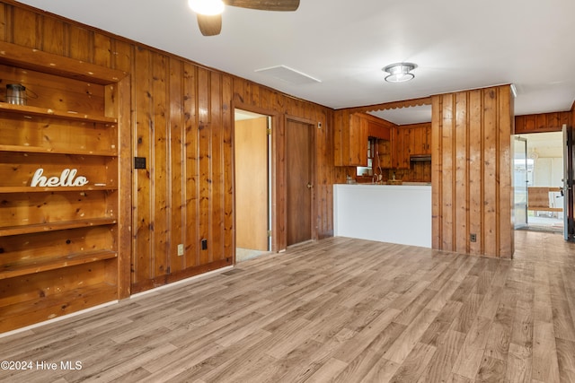 unfurnished living room featuring built in shelves, light wood-type flooring, wooden walls, and ceiling fan