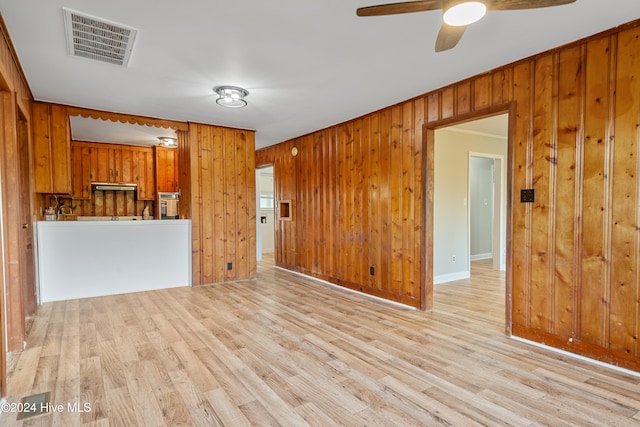 unfurnished living room featuring wooden walls, ceiling fan, and light hardwood / wood-style flooring