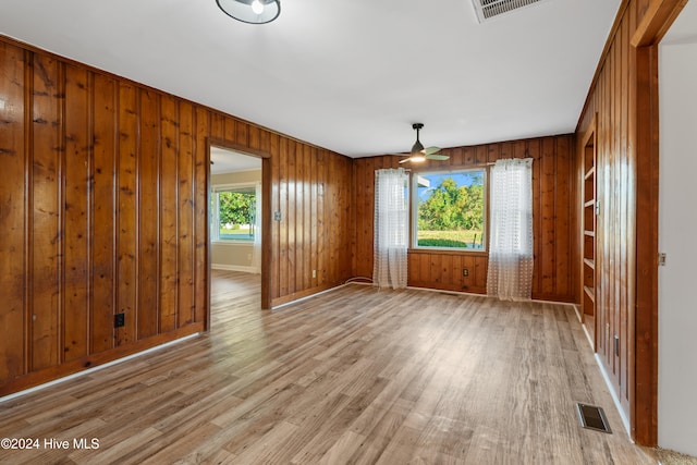 unfurnished room featuring light wood-type flooring, wood walls, and ceiling fan