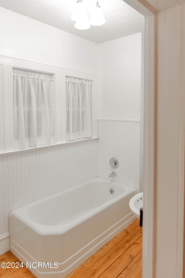 bathroom with a textured ceiling, a bath, and hardwood / wood-style floors