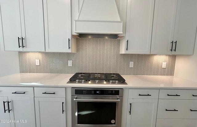 kitchen with white cabinetry, appliances with stainless steel finishes, custom range hood, and backsplash