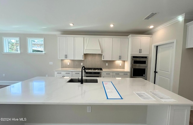 kitchen featuring sink, a large island with sink, double oven, white cabinets, and backsplash