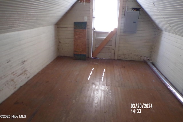 bonus room featuring lofted ceiling, hardwood / wood-style floors, electric panel, and wooden walls