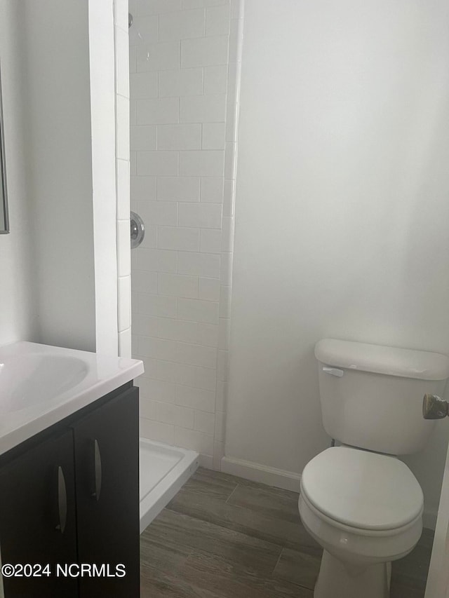 bathroom featuring tiled shower, vanity, toilet, and hardwood / wood-style flooring