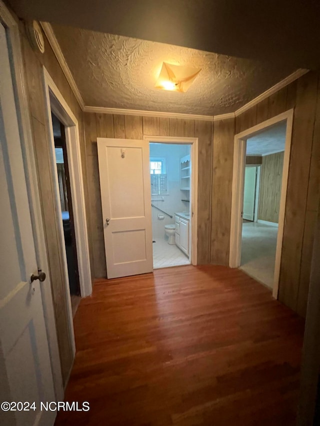 corridor with ornamental molding, wooden walls, a textured ceiling, and hardwood / wood-style floors