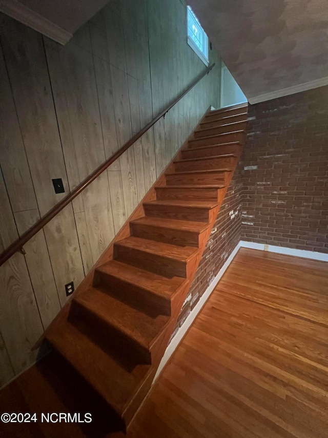 stairway featuring ornamental molding, wood-type flooring, brick wall, and wooden walls