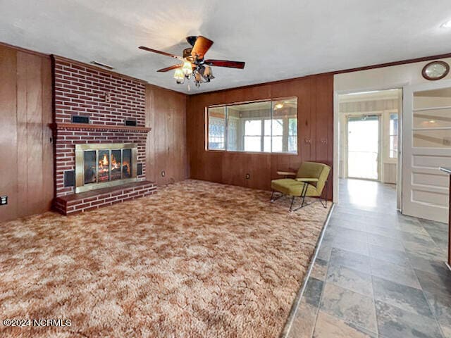 unfurnished living room featuring wood walls, ceiling fan, and a fireplace