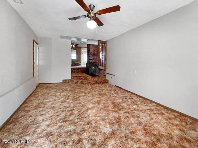 carpeted empty room with ceiling fan and a wood stove