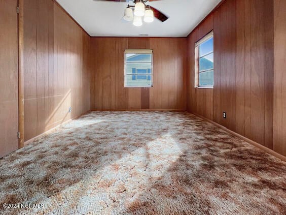 spare room featuring ceiling fan, wood walls, and carpet