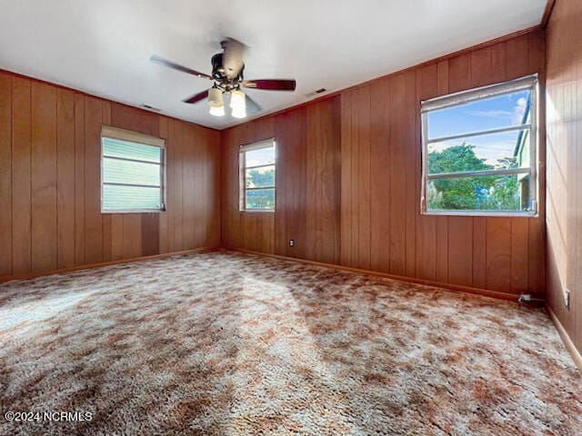 unfurnished room featuring wooden walls, ceiling fan, and a wealth of natural light