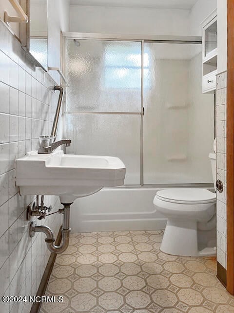 bathroom featuring tile walls, backsplash, tile patterned floors, enclosed tub / shower combo, and toilet