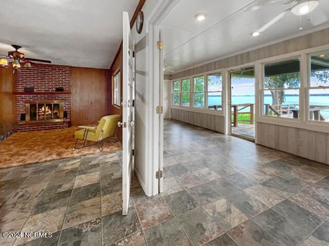 interior space with crown molding, wooden walls, ceiling fan, and a brick fireplace