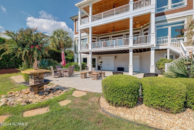 back of property featuring ceiling fan, a fire pit, a balcony, and a patio area