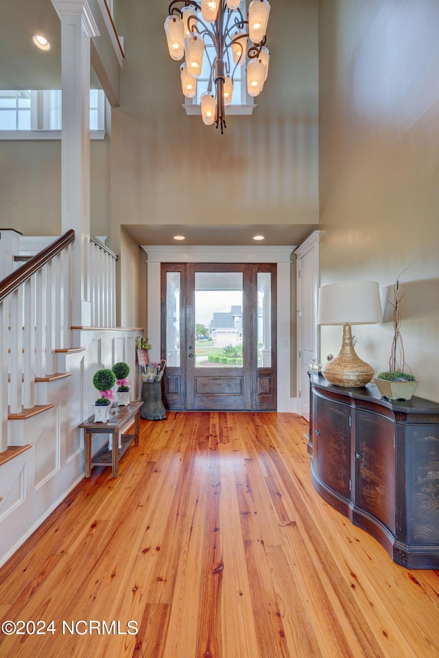 entryway featuring a notable chandelier, light hardwood / wood-style flooring, decorative columns, and a high ceiling