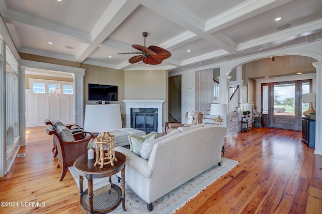 living room with light wood-type flooring, beamed ceiling, ceiling fan with notable chandelier, coffered ceiling, and ornamental molding