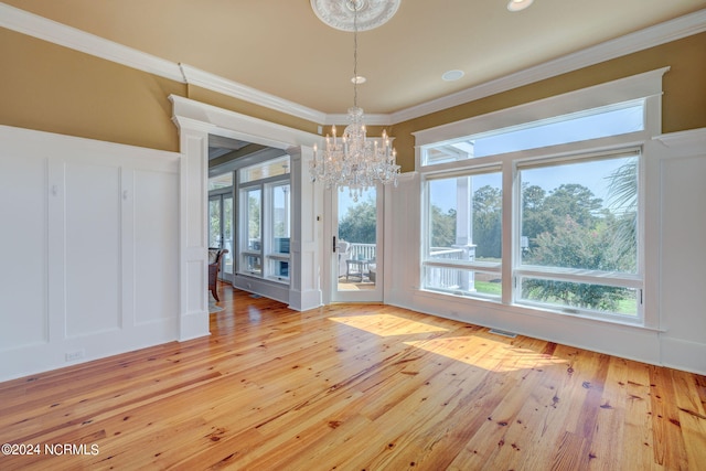 unfurnished dining area with light wood-type flooring, a chandelier, ornamental molding, and a wealth of natural light