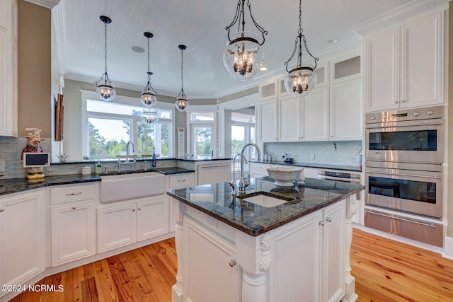 kitchen with stainless steel double oven, sink, an island with sink, and plenty of natural light