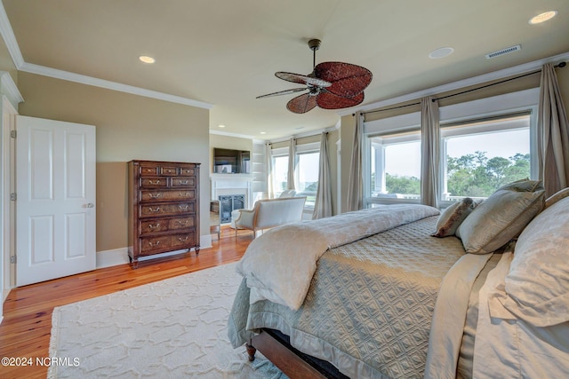 bedroom with crown molding, wood finished floors, a glass covered fireplace, visible vents, and recessed lighting