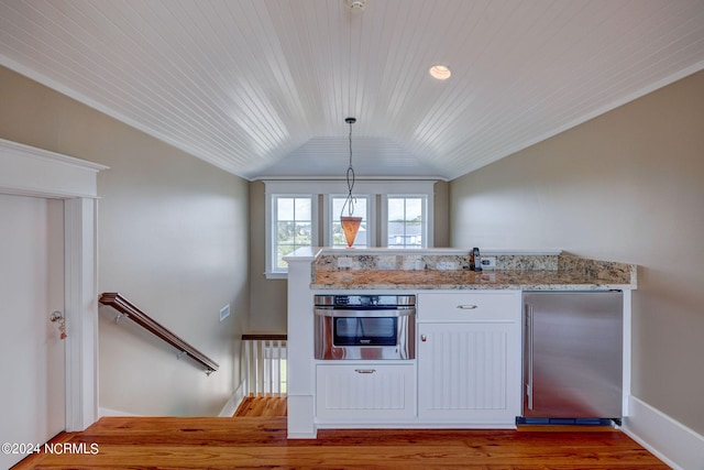 kitchen with pendant lighting, wood-type flooring, light stone counters, lofted ceiling, and appliances with stainless steel finishes