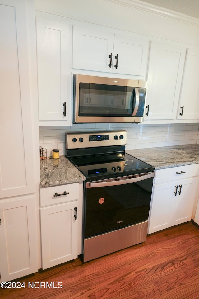 kitchen with white cabinets, tasteful backsplash, wood-type flooring, stainless steel appliances, and light stone countertops