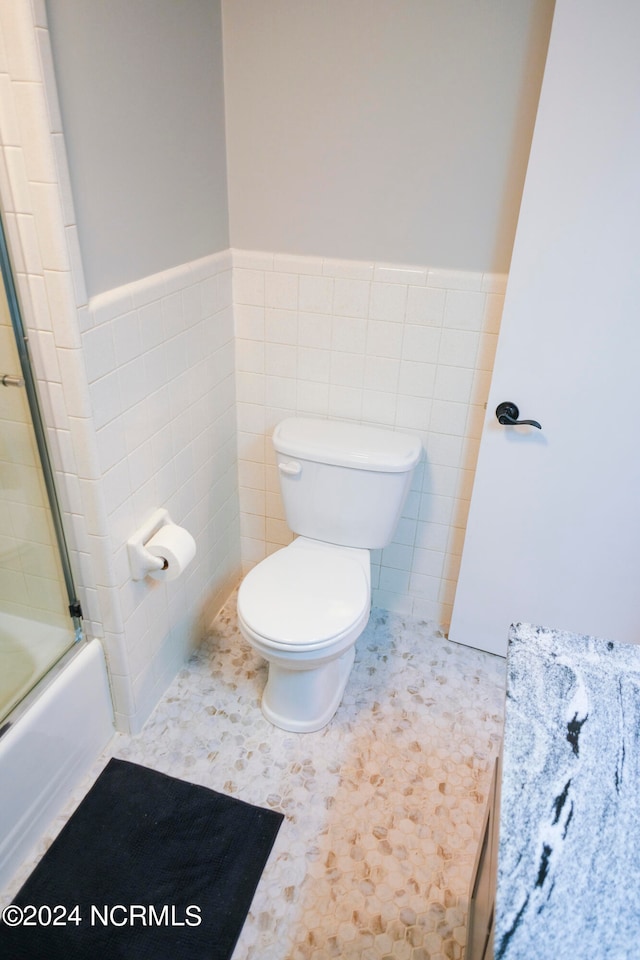 bathroom with bath / shower combo with glass door, tile walls, toilet, and tile patterned floors