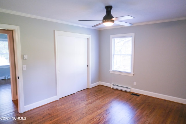 unfurnished bedroom featuring baseboard heating, a closet, wood-type flooring, crown molding, and ceiling fan