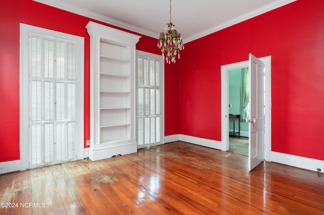 empty room featuring wood-type flooring, a chandelier, ornamental molding, and built in features