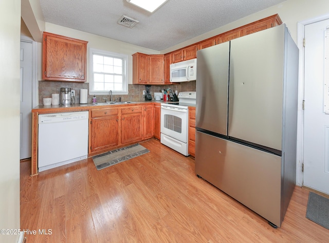 kitchen featuring sink, decorative backsplash, white appliances, a textured ceiling, and light hardwood / wood-style flooring