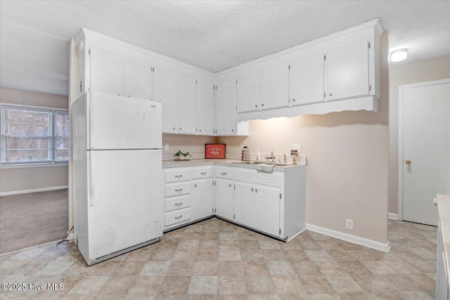 kitchen with white refrigerator, sink, white cabinets, and a textured ceiling