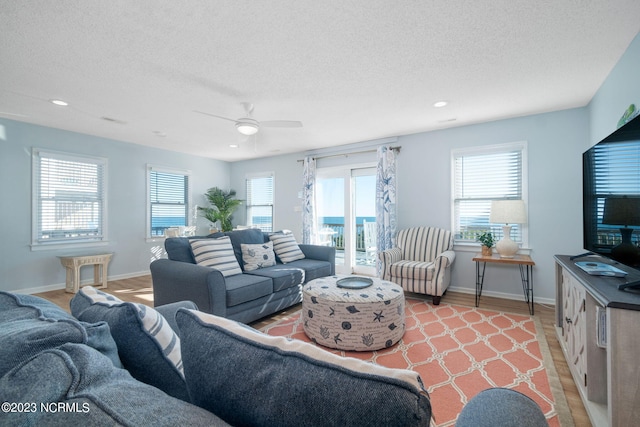 living room with ceiling fan, a textured ceiling, and light wood-type flooring