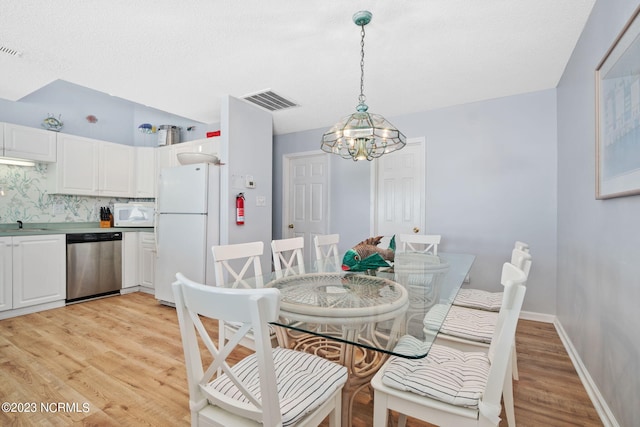 dining space with a textured ceiling, a notable chandelier, and light hardwood / wood-style floors