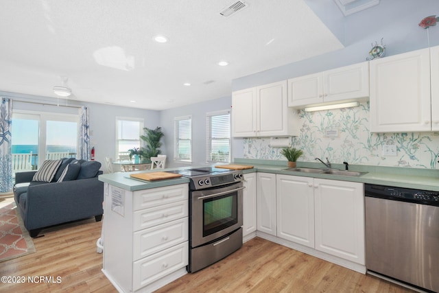 kitchen with sink, white cabinetry, appliances with stainless steel finishes, kitchen peninsula, and light hardwood / wood-style floors