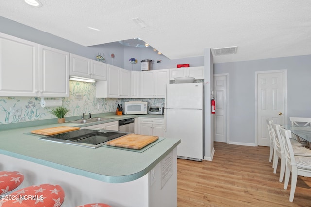 kitchen with white cabinetry, white appliances, kitchen peninsula, and sink