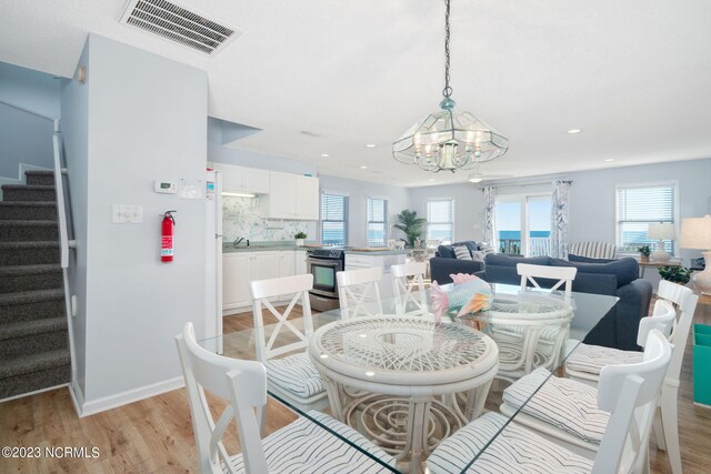 dining area featuring sink, light wood-type flooring, and an inviting chandelier