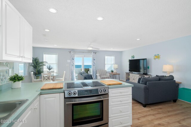 kitchen featuring stainless steel electric stove, a wealth of natural light, light wood-type flooring, and white cabinets