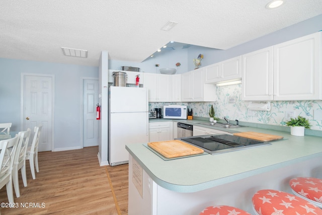 kitchen featuring light hardwood / wood-style flooring, kitchen peninsula, sink, white cabinetry, and white appliances