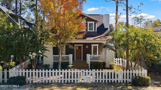 view of front facade with roof with shingles, a fenced front yard, and a porch