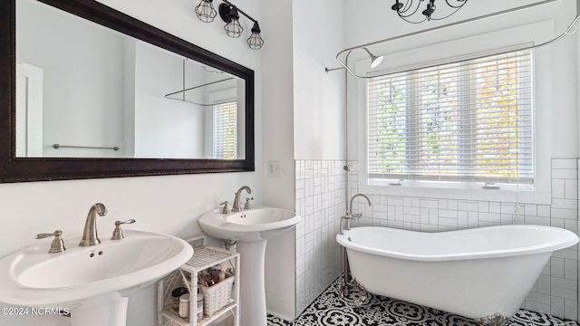 full bath featuring a freestanding tub, tile walls, tile patterned flooring, wainscoting, and a sink