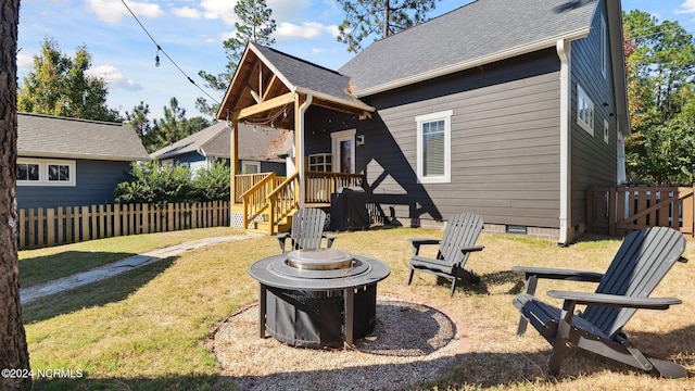 rear view of property featuring a lawn, crawl space, fence, and an outdoor fire pit