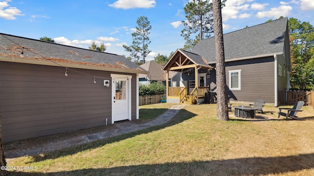 back of house featuring fence, a yard, an outdoor fire pit, and roof with shingles