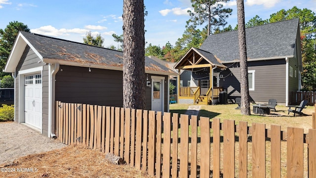 view of front of home with fence private yard, a fire pit, a shingled roof, an outbuilding, and a detached garage